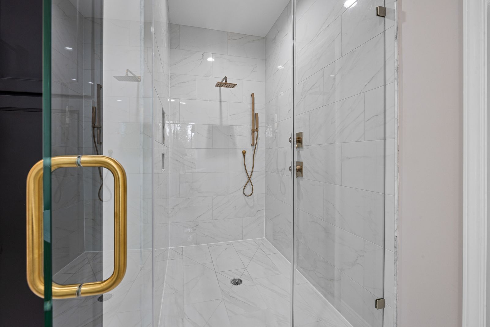Glass shower enclosure with a brass handle, marble tiles and a rain head