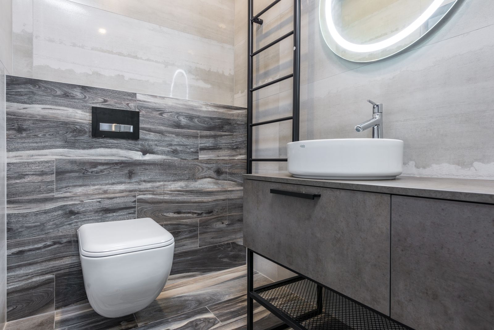 Wall-hung toilet with a concealed flush plate in a grey tiled bathroom