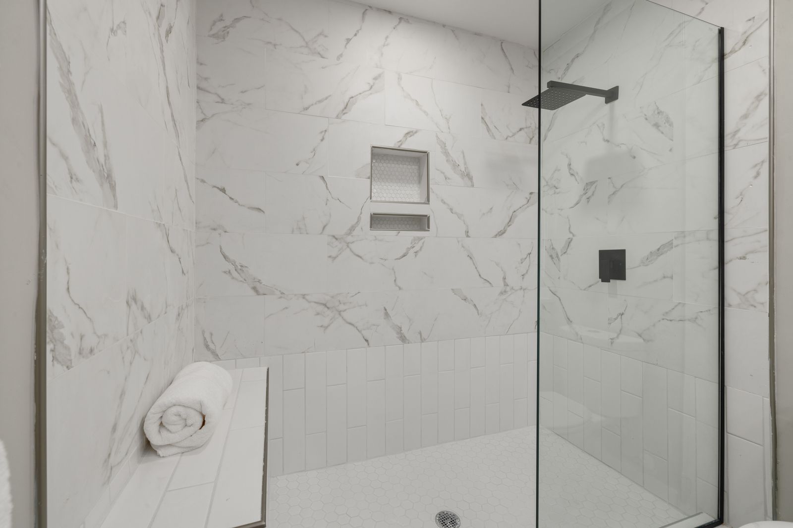 White marble walk-in shower with a glass screen, black fixtures and a bench